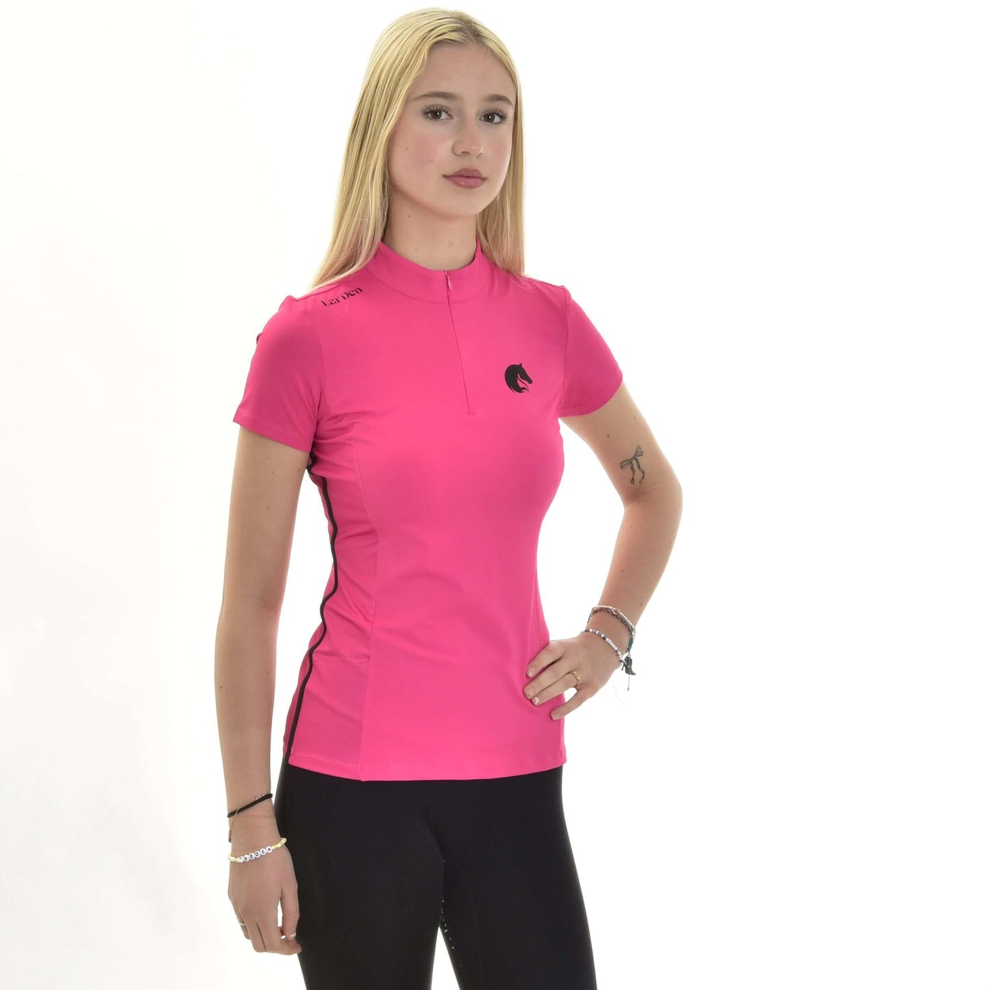 Športové tričko LarDen Pink od Hobby Horse LarDen, žiarivo ružový športový top s krátkym rukávom zo spandexu, predvádza mladá žena s dlhými blond vlasmi, v kombinácii s čiernymi nohavicami, pózujúca na čisto bielom pozadí s jednou rukou v páse.