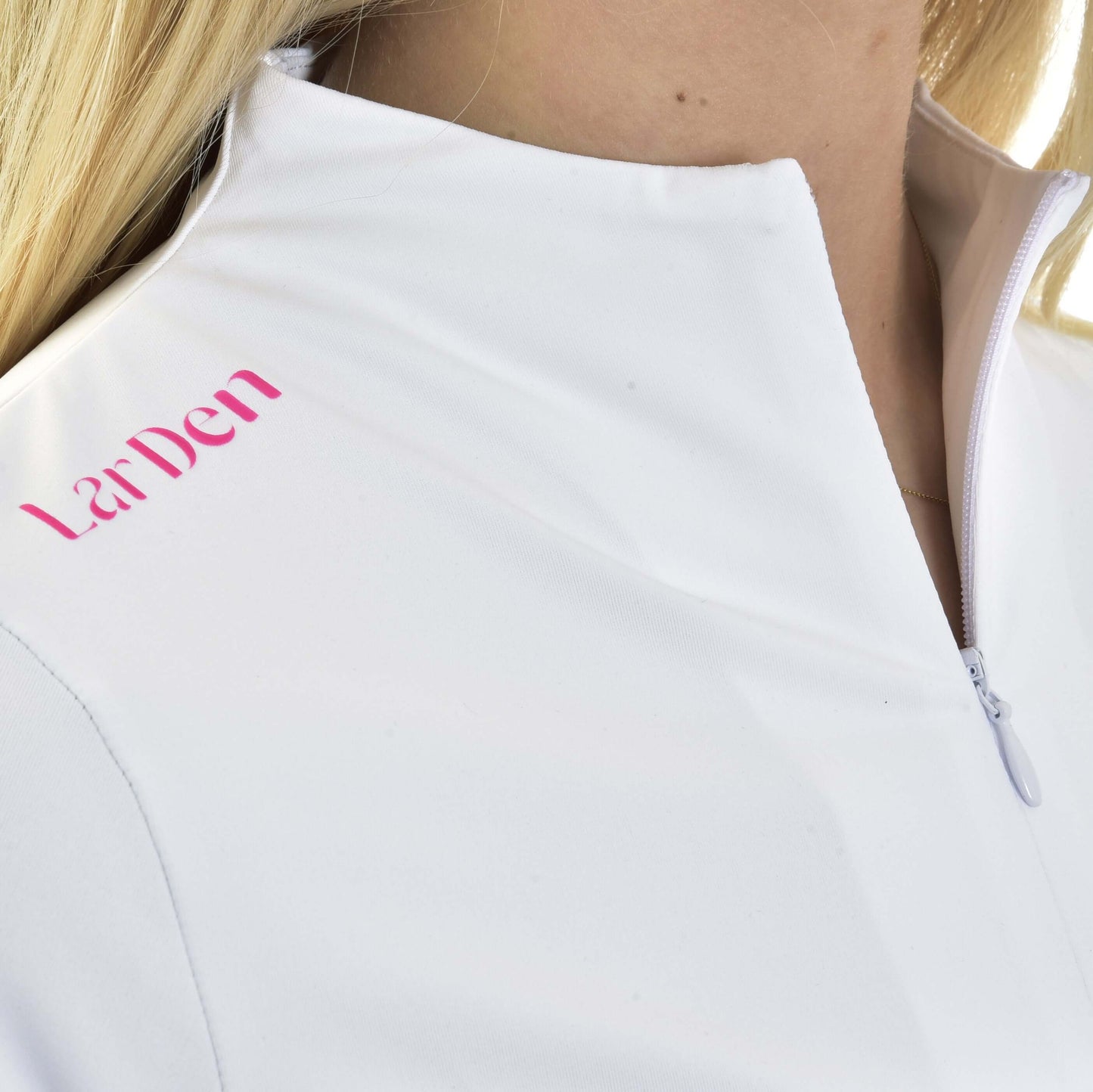 Detail blond osoby v Športovom tričku LarDen Premium od Hobby Horse LarDen, bielom športovom tričku na zips s ružovým nápisom „LarDen“ na ramene. Spandexová tkanina zaisťuje pohodlie.