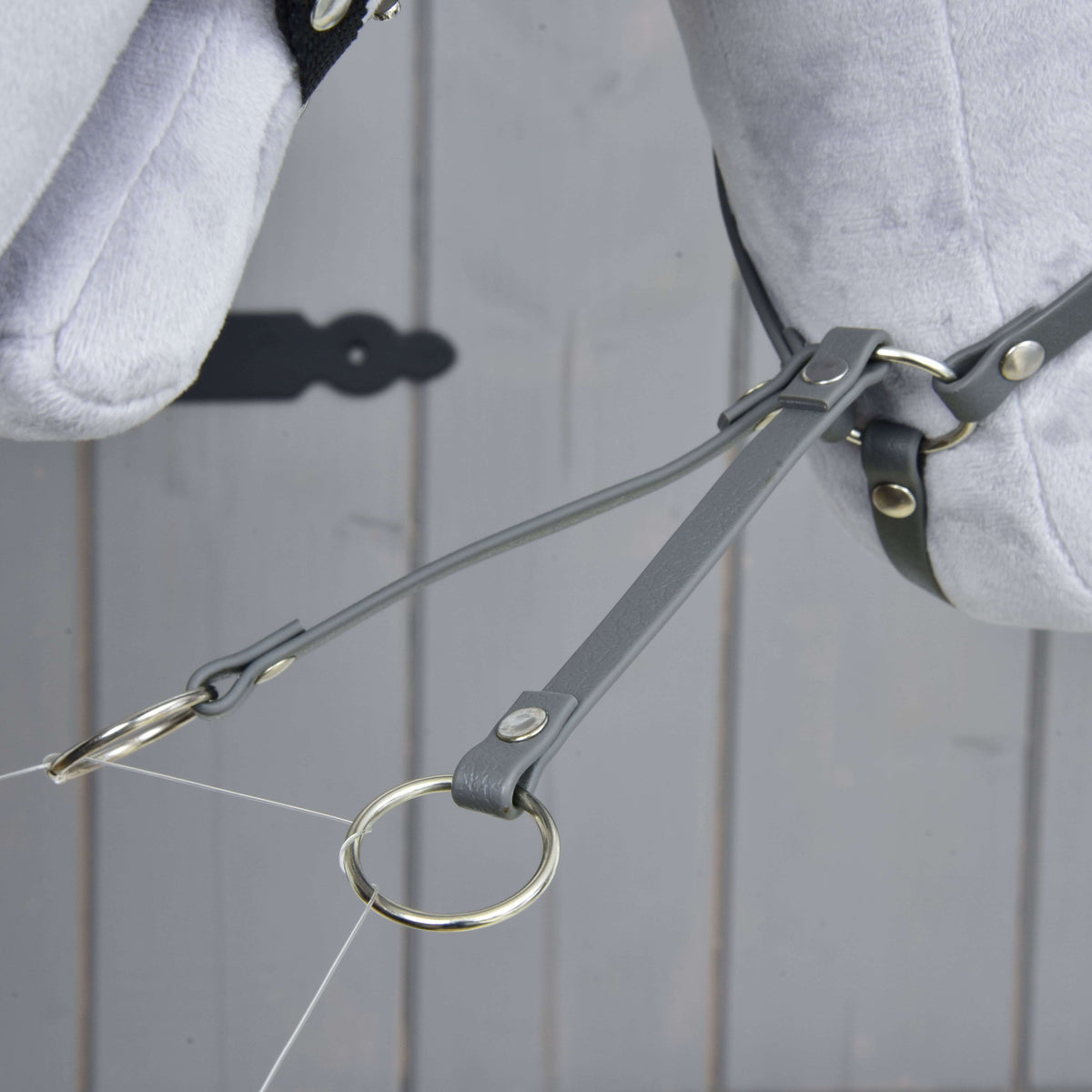 Martingal tmavosivý od Hobby Horse LarDen, detail sivých kožených remienkov a koženkového martingalu s kovovými krúžkami na svetlosivej plyšovej konskej hlave na drevenom pozadí.