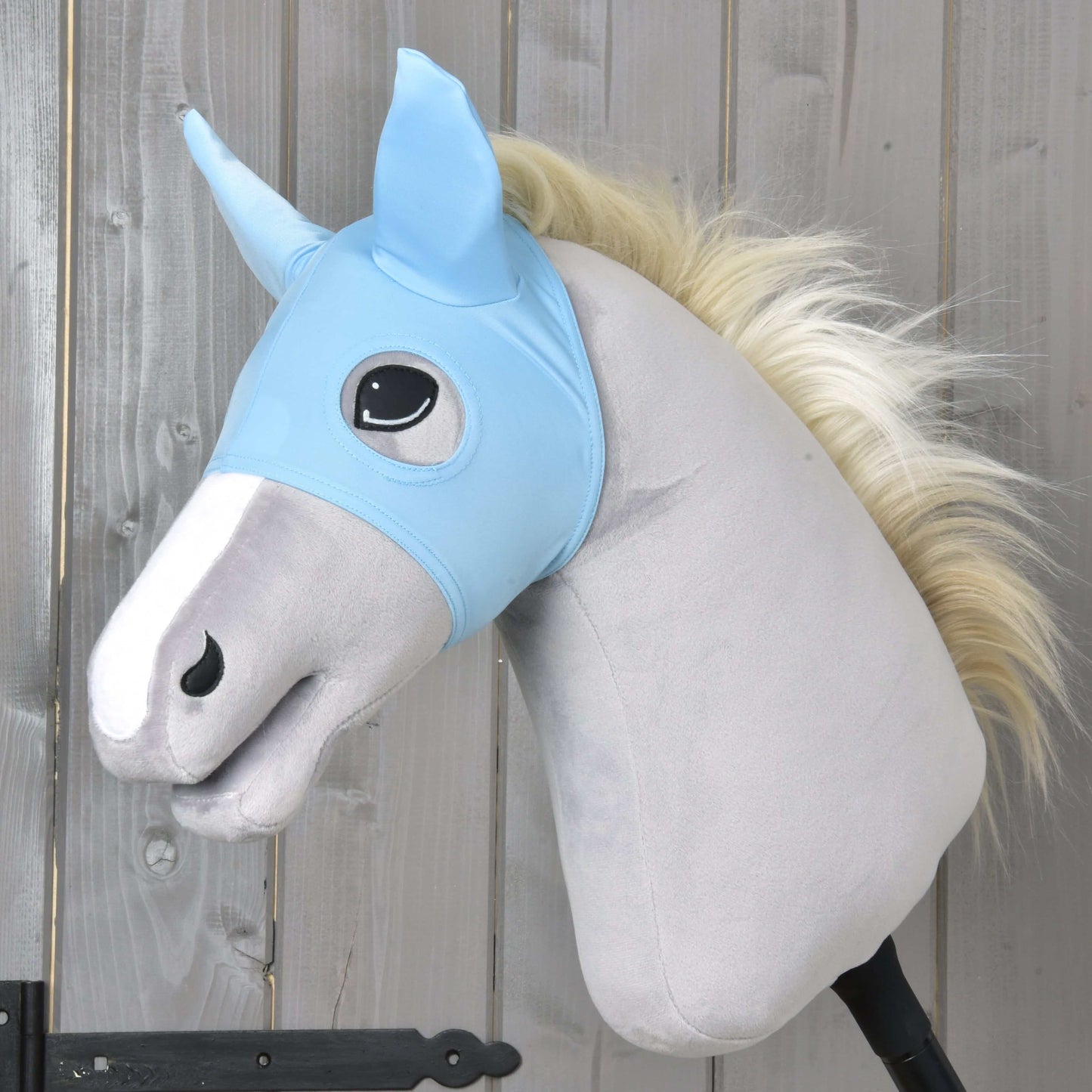 Maska Sky od Hobby Horse LarDen na svetlosivom plyšovom Hobby Horse s bielou hrivou, svetlomodrou látkovou uzdečkou, čiernou rukoväťou tyče a prateľnou maskou, zobrazená na pozadí drevených panelov.