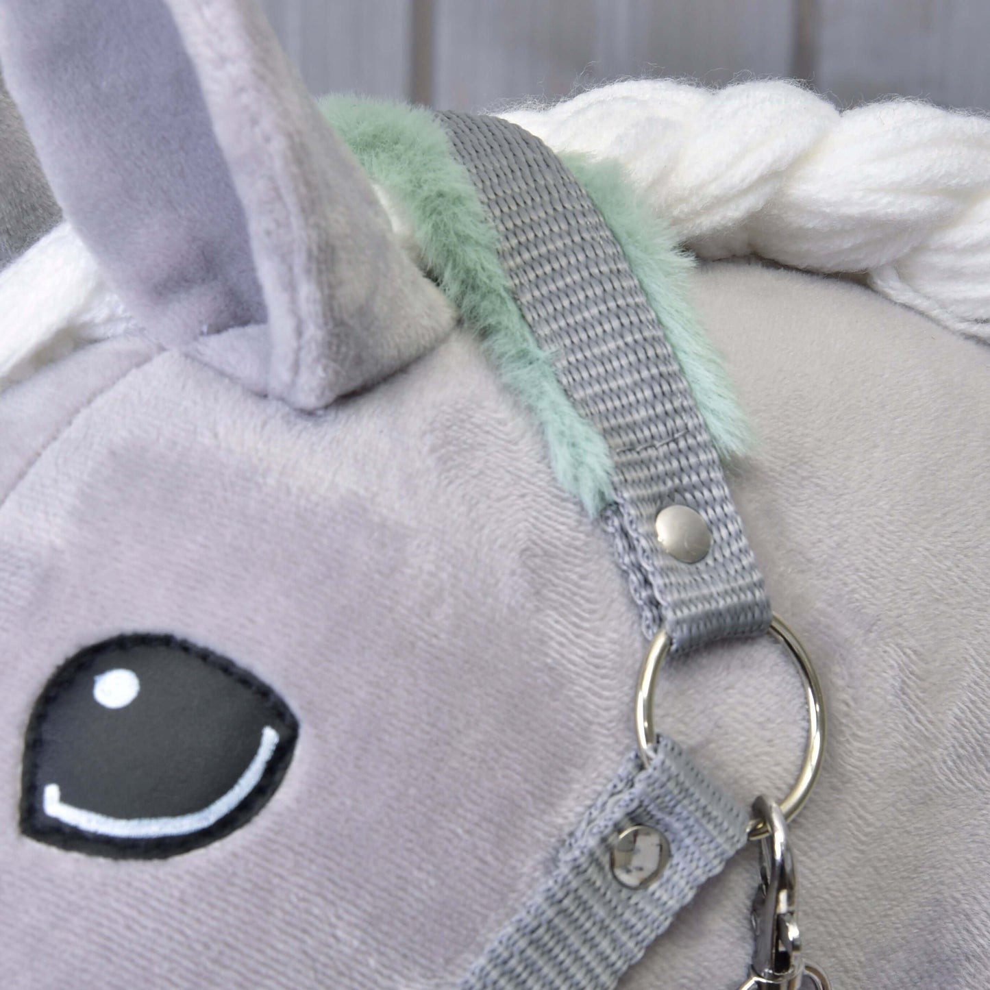 Detailný záber sivého plyšového jednorožca s čiernobielym vyšívaným okom, bielou priadzovou hrivou, mint zelenými akcentmi a Hobby Horse LarDen "Ohlávkou sivou s mint barančekom" so strieborným krúžkom a zapínaním.