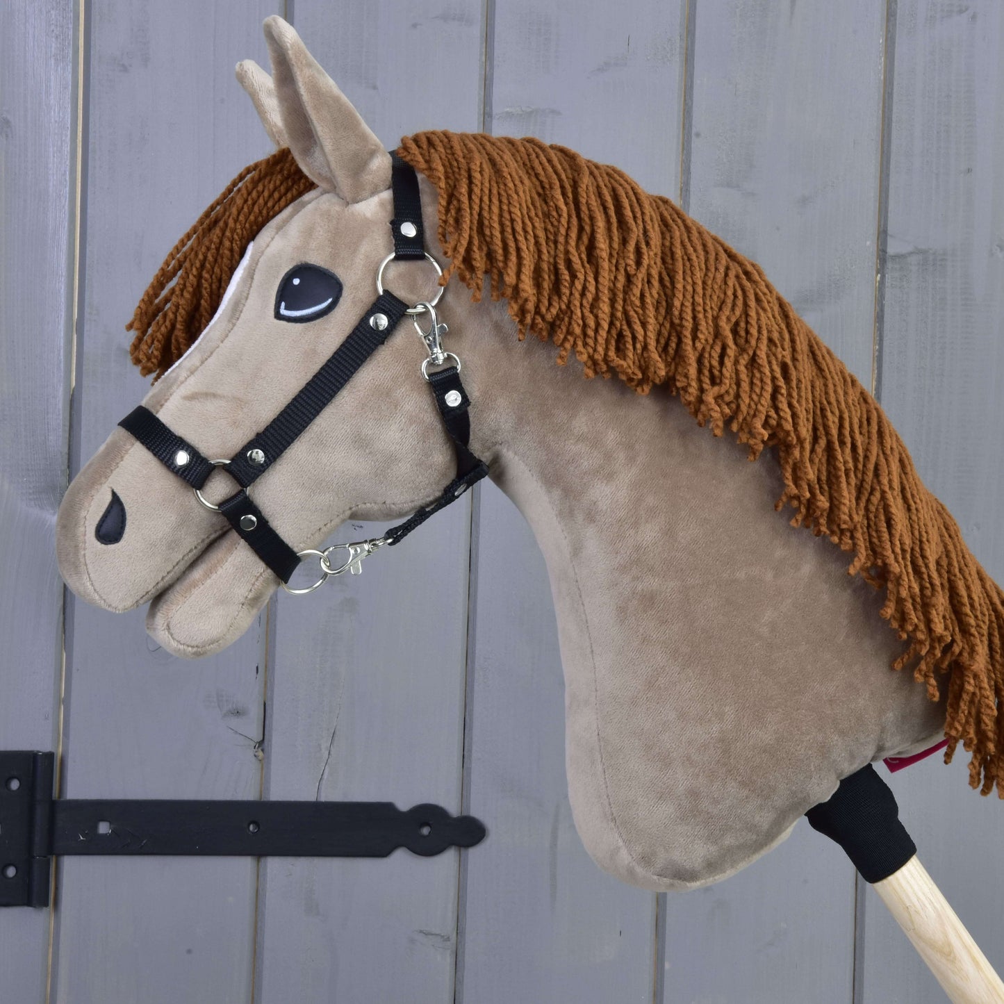 Hobby Horse Oliver s čiernou ohlávkou + ohlávkou s barančekom ZADARMO od Hobby Horse LarDen stojí pred sivou drevenou stenou.