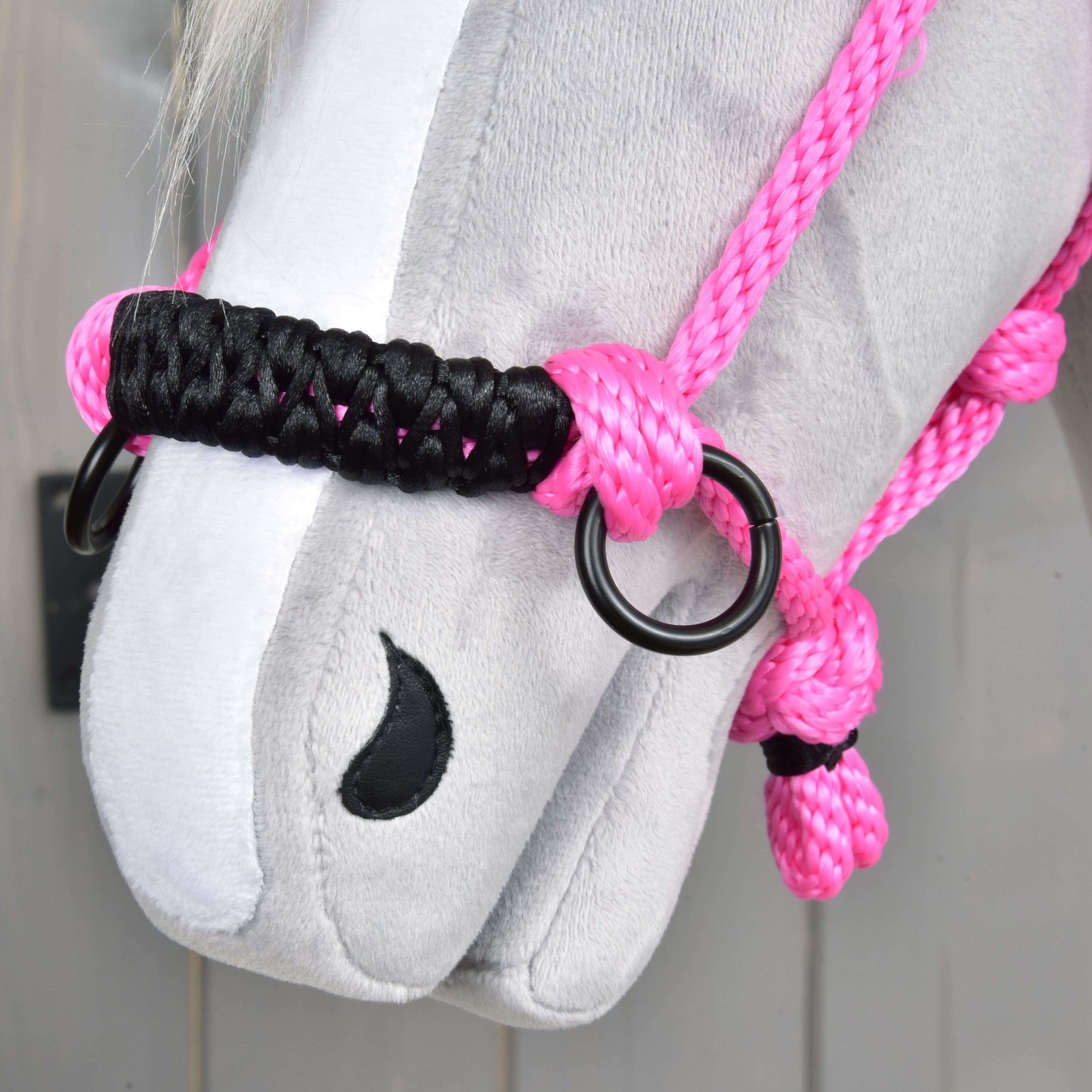 Detail tváre sivého plyšového koňa s Parelka Pink od Hobby Horse LarDen s výrazným ružovým lanom, čiernymi a ružovými uzlami, kovovými krúžkami a čierne prešitou nozdrou.