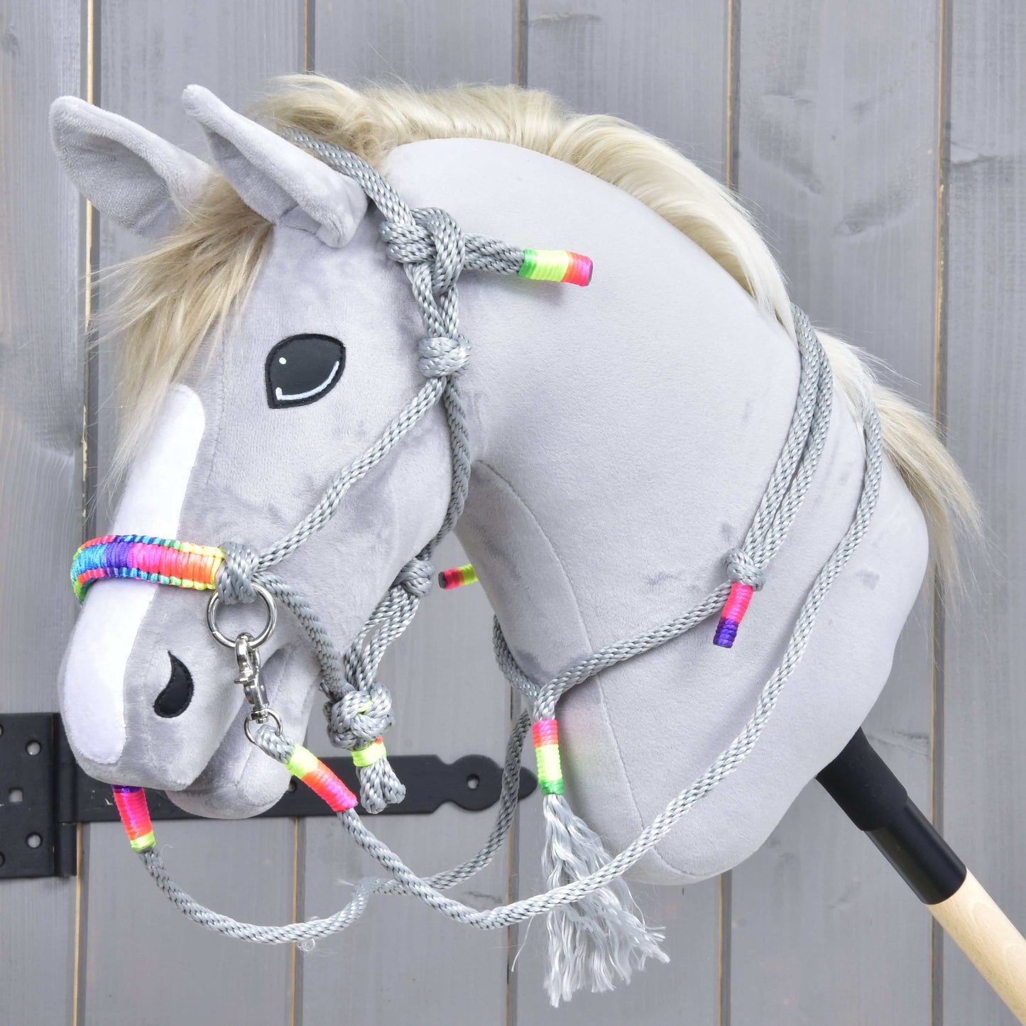 Sivý Hobby Horse s bielou lysinou, čiernym nosom a blond hrivou má na sebe Povrazový set Manhattan od Hobby Horse LarDen so sivou povrazovou ohlávkou a opratami s farebnými korálikmi, na drevenom pozadí.