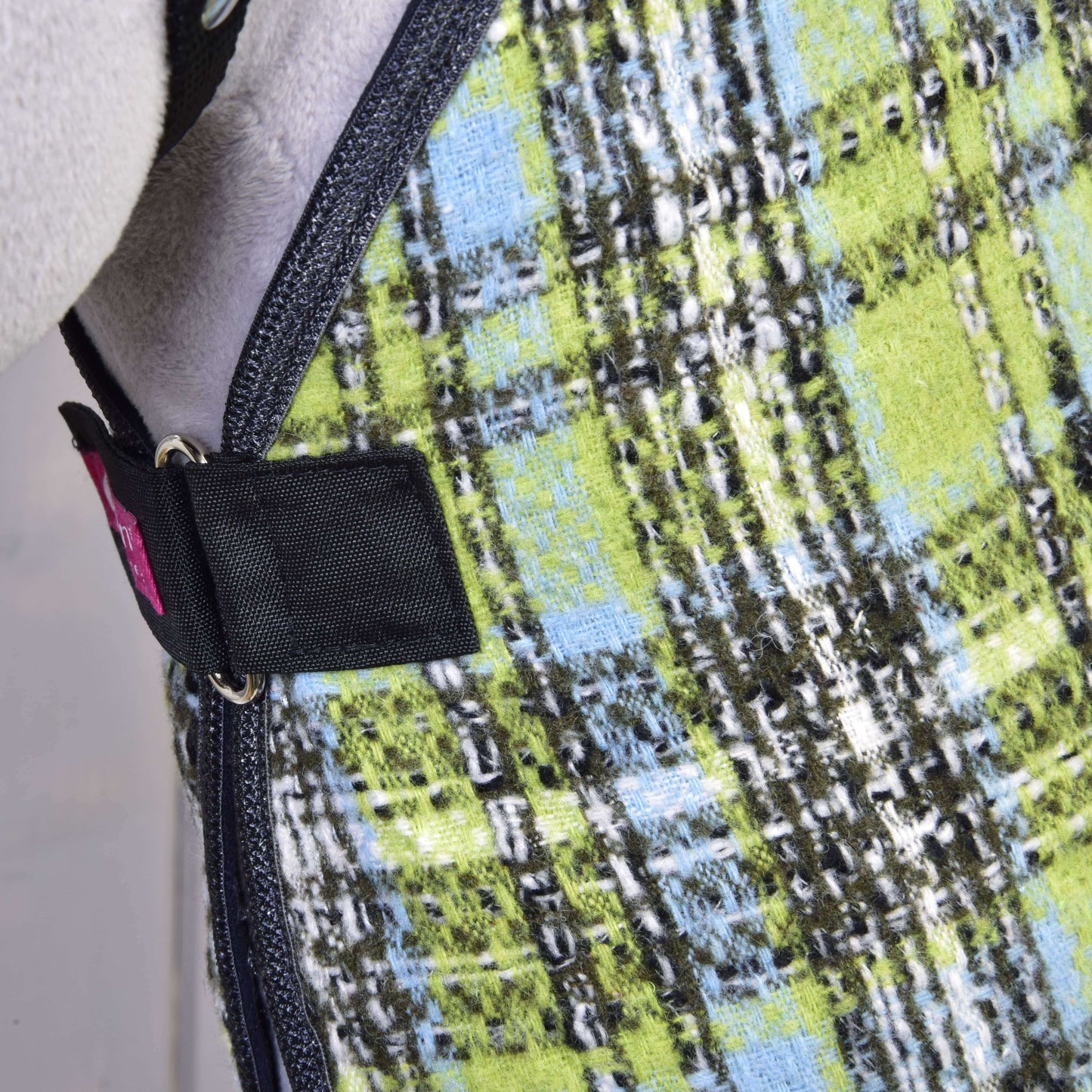 Detail deky Deka stajňová Lemon Blue od Hobby Horse LarDen, zobrazujúci zelenú, modrú, čiernu a bielu károvanú látku s čiernym popruhom a kovovou prackou – ideálna pre ochranu koňa alebo tréning.