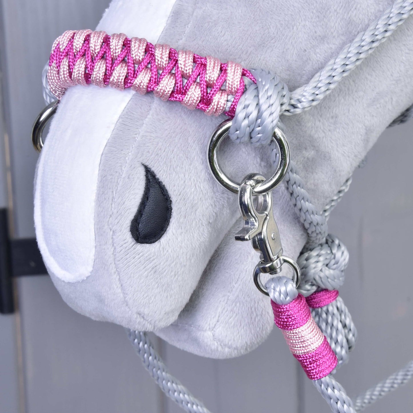 Detail sivej plyšovej hlavy Hobby Horse LarDen s Povrazovým setom Rosie: ružovo-strieborná pletená ohlávka a vodidlo, čierne vyšívané oko a kovová karabína na svetlom drevenom pozadí.