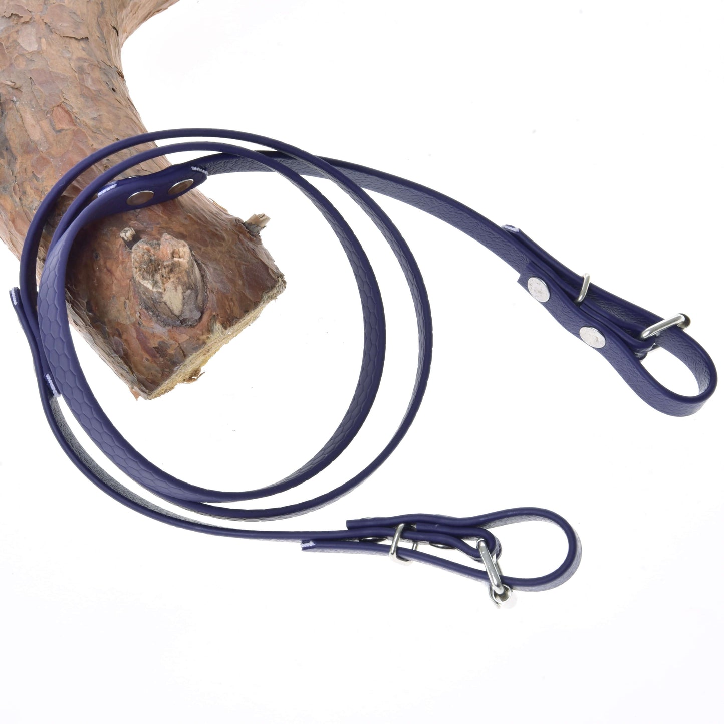 Otěže pogumované Dark purple od Hobby Horse LarDen jsou zobrazené stočené na bílém povrchu, částečně přehozené přes strukturované dřevo, připomínající eleganci klasických jezdeckých uzdeček.