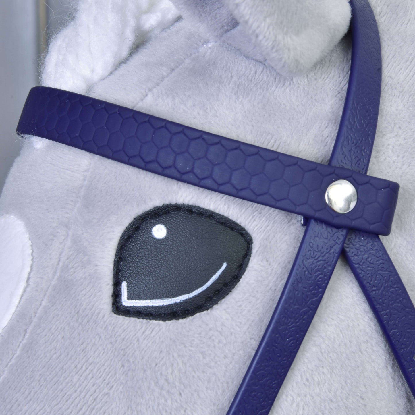 Detail tváre plyšového koňa s vyšitým čierno-bielym okom, s Kompletná uzdečka s nánosníkom Dark Purple od Hobby Horse LarDen; uzdečka má strieborný gombíkový detail a srsť koňa je svetlosivá.