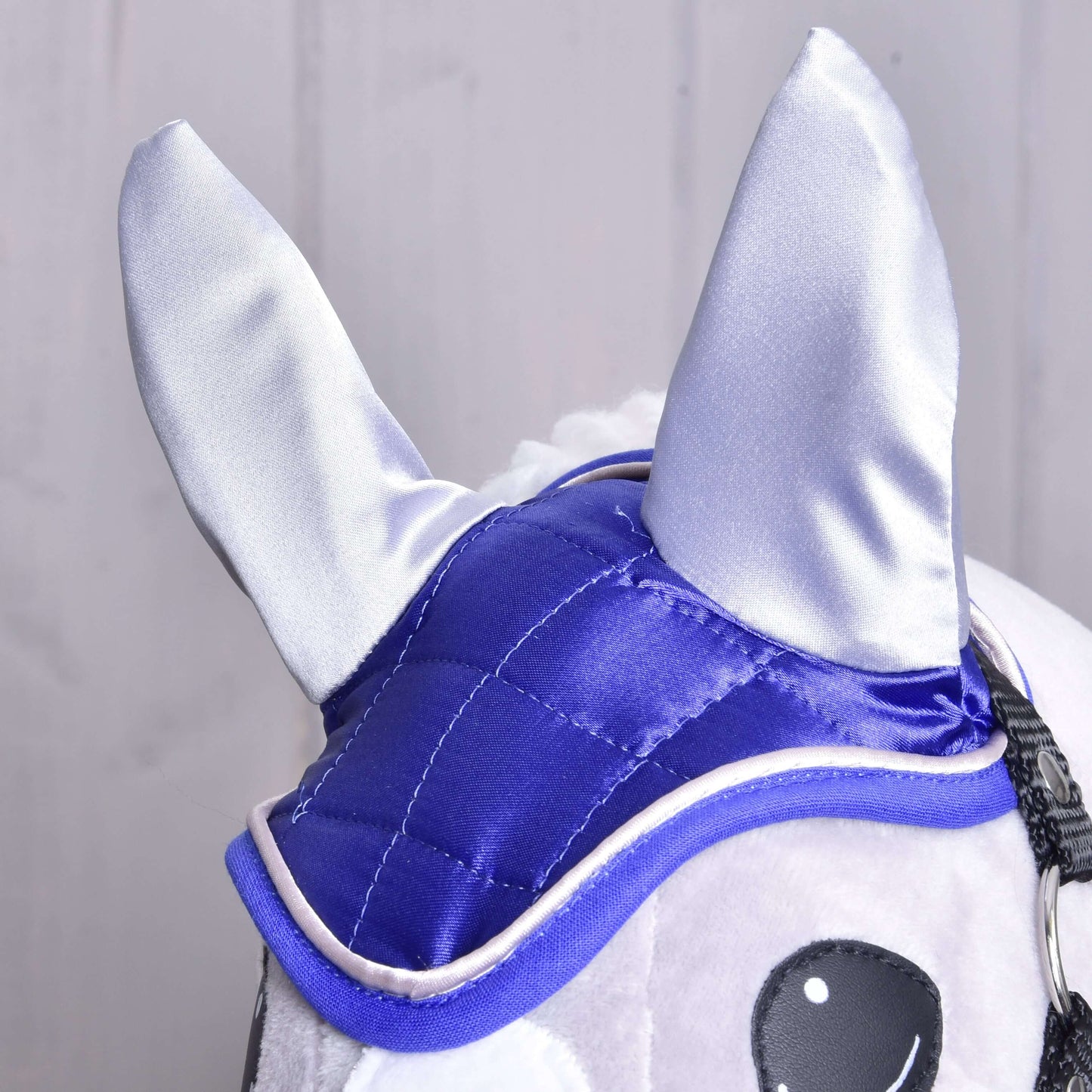 Detail čabraky DeLuxe Blue od Hobby Horse LarDen na plyšovom Hobby Horse, s lesklou modrou a striebornou látkou pre ochranu proti hmyzu, veľkými špicatými ušami a čiernobielo vyšívanými očami na svetlom pozadí.
