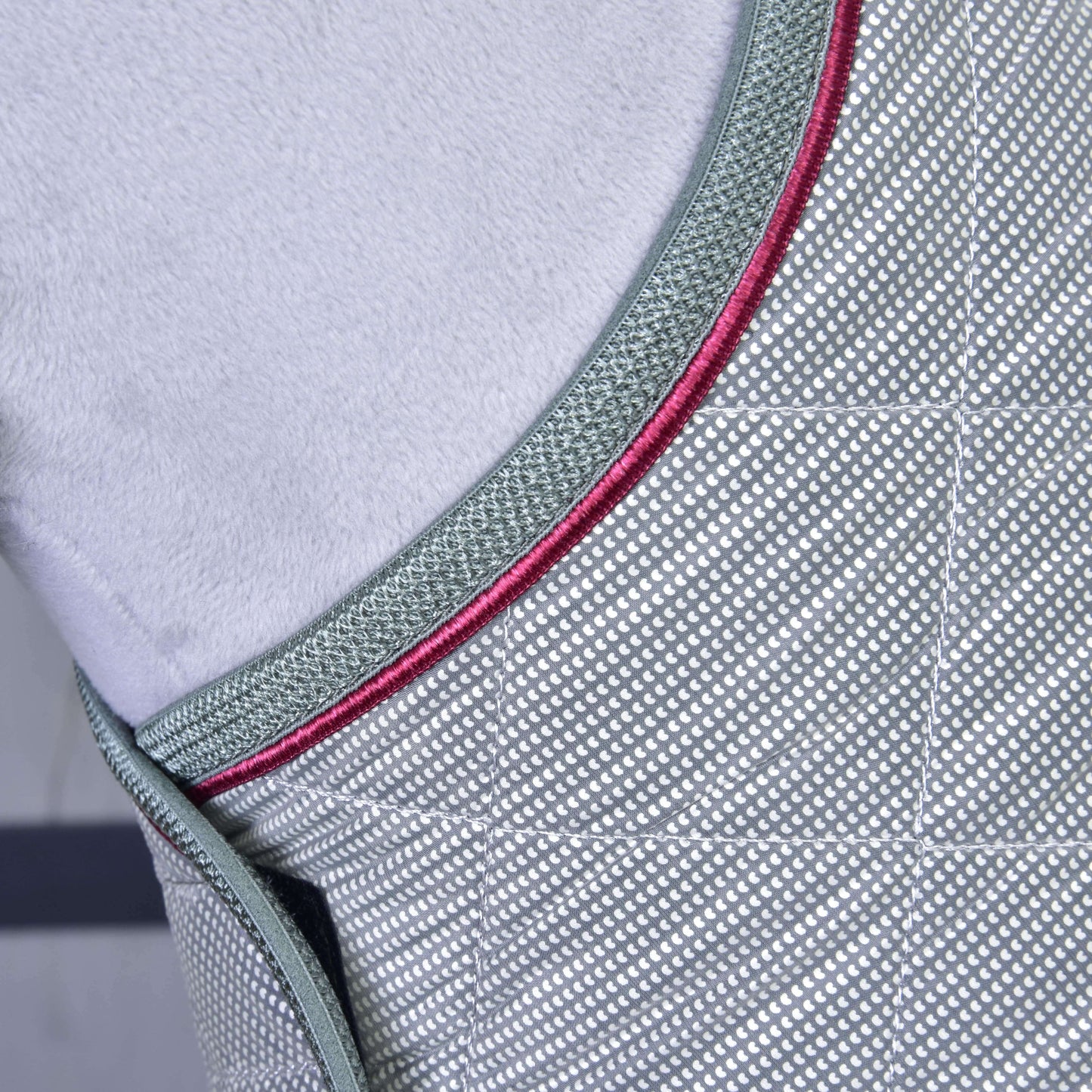 Detail deky Silver Eleganza od Hobby Horse LarDen: sivá tréningová deka s kosoštvorcovým vzorom, tmavozeleným lemovaním a červenými akcentmi. Mäkké svetlosivé pozadie zvýrazňuje jej detailné prešívanie pre optimálnu ochranu koňa.