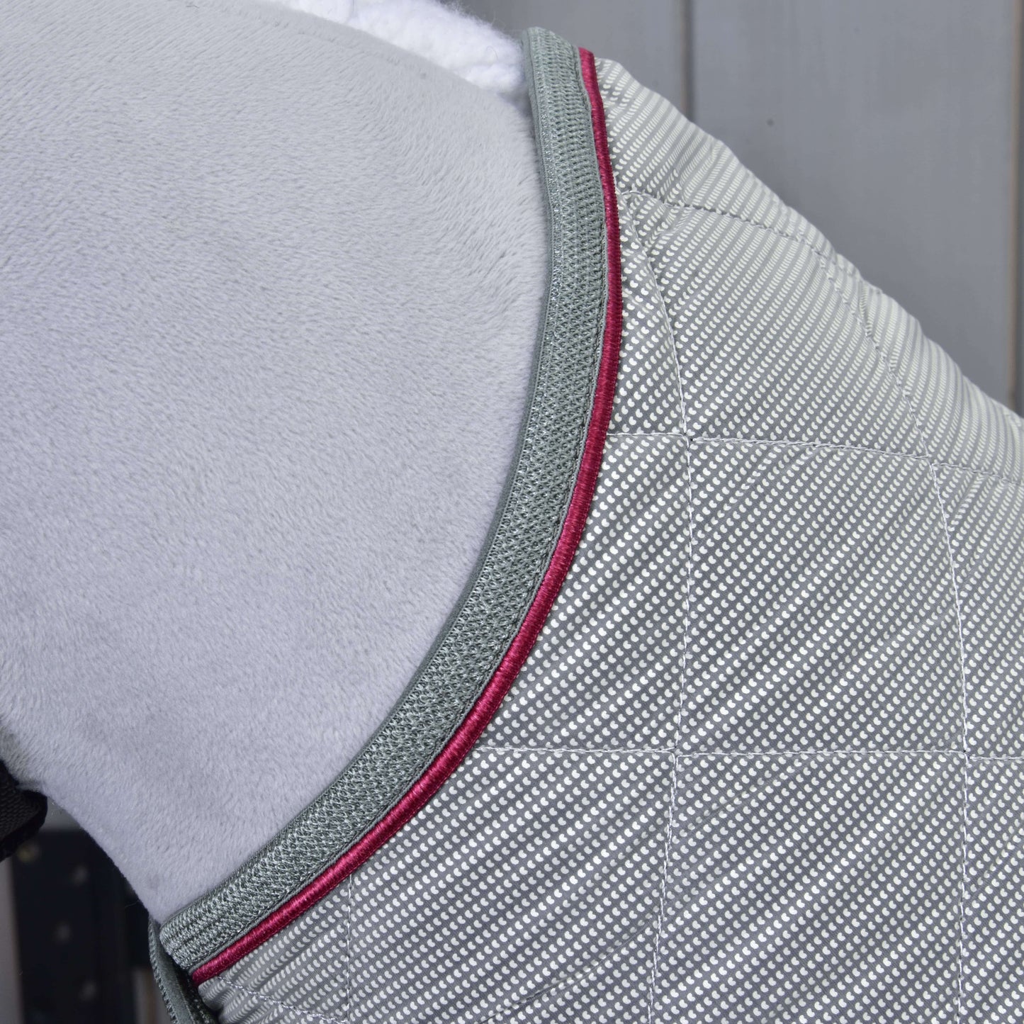 Detail Hobby Horse LarDen Deka Silver Eleganza, svetlosivej prešívanej tréningovej deky s mriežkovým vzorom, sivým lemovaním a tmavoružovou paspulkou, prehodenej cez mäkký biely povrch.