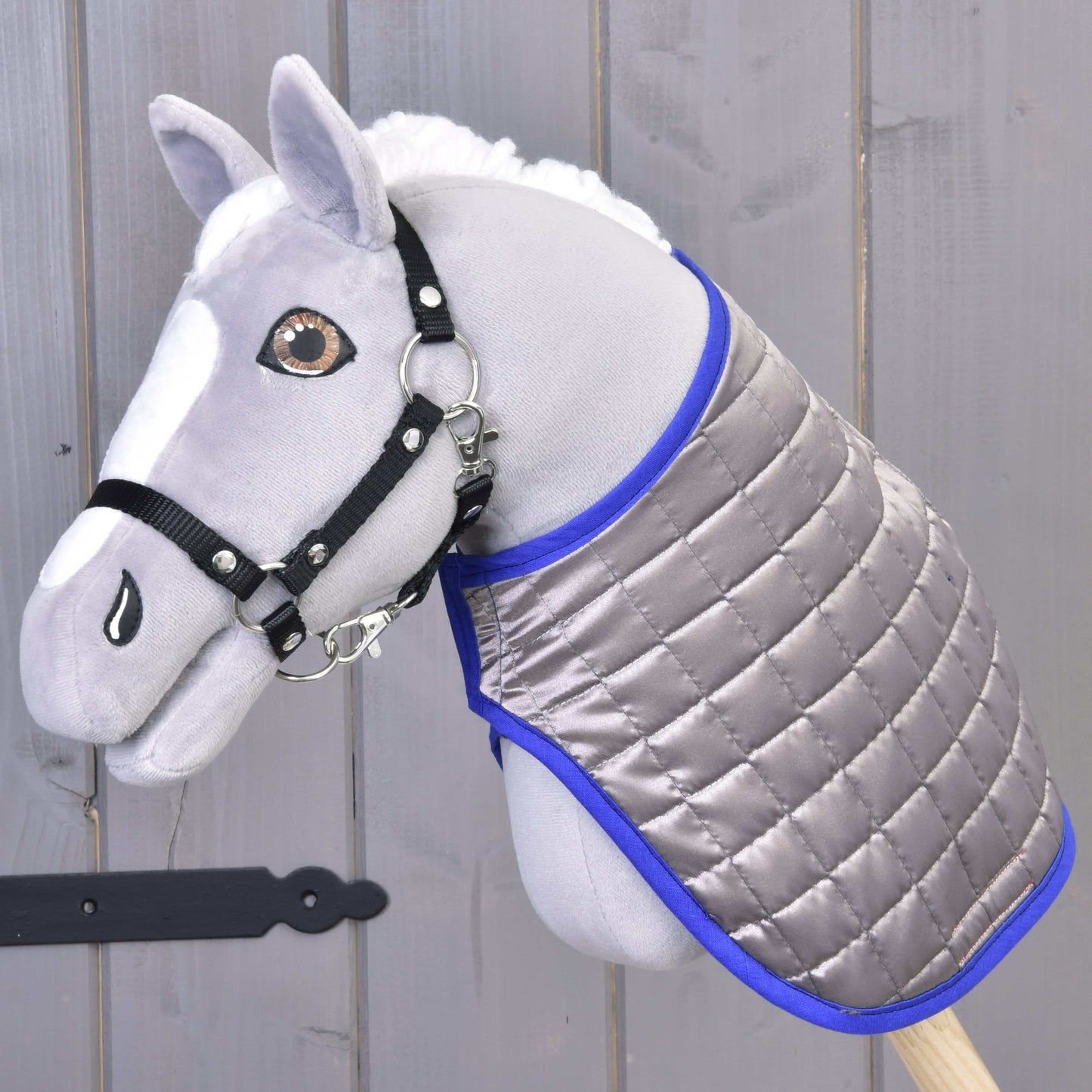 Šedý plyšový Hobby Horse s černou uzdečkou a oboustrannou dekou Deka DeLuxe Blue od Hobby Horse LarDen na pozadí šedého dřeva.