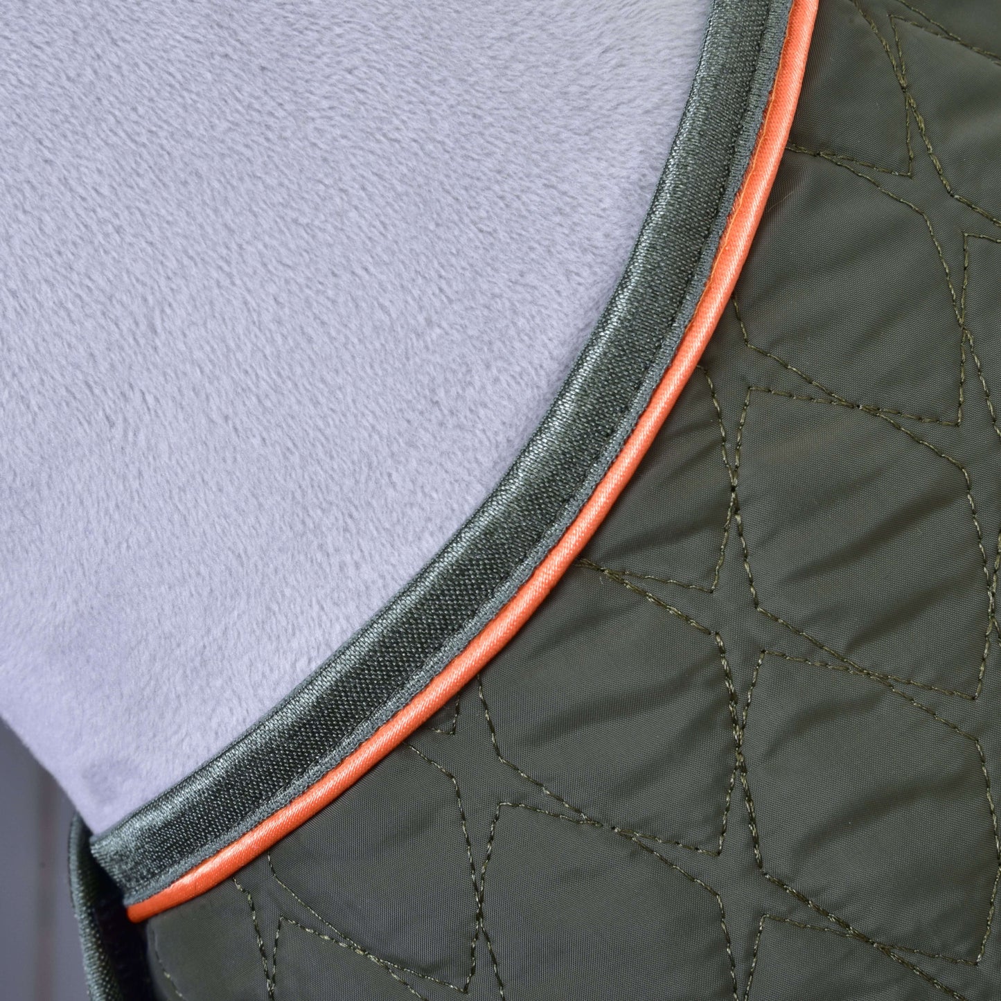 Deka Sport od Hobby Horse LarDen, prešívaná zelená ochranná konská deka s oranžovým lemovaním a viditeľným prešívaním, zobrazená zblízka na mäkkom svetlosivom štruktúrovanom povrchu.