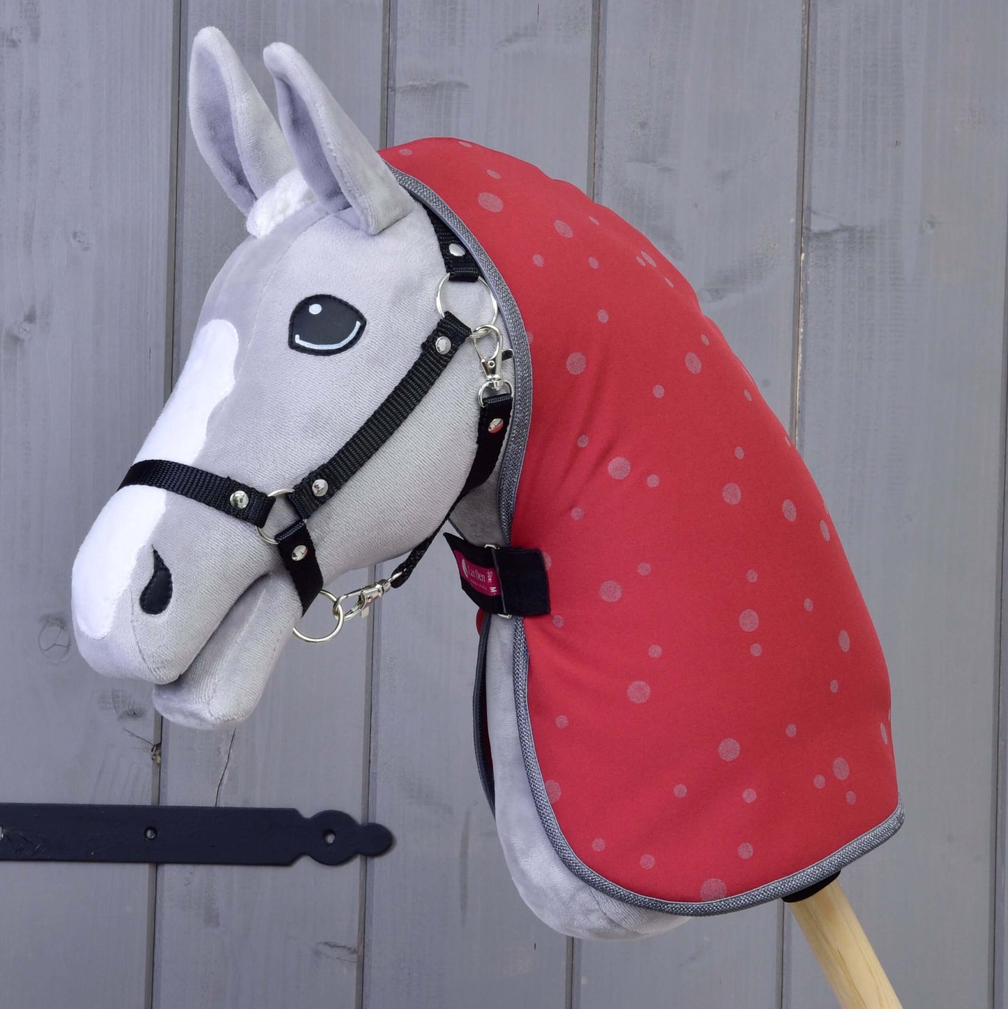 Hobby Horse LarDen plyšový Hobby Horse s čiernou uzdečkou a dekou Deka stajňová Raspberry, nasadený na drevenej tyči — ideálny pre nápaditú hru a tréning s koňom pred akýmkoľvek pozadím.