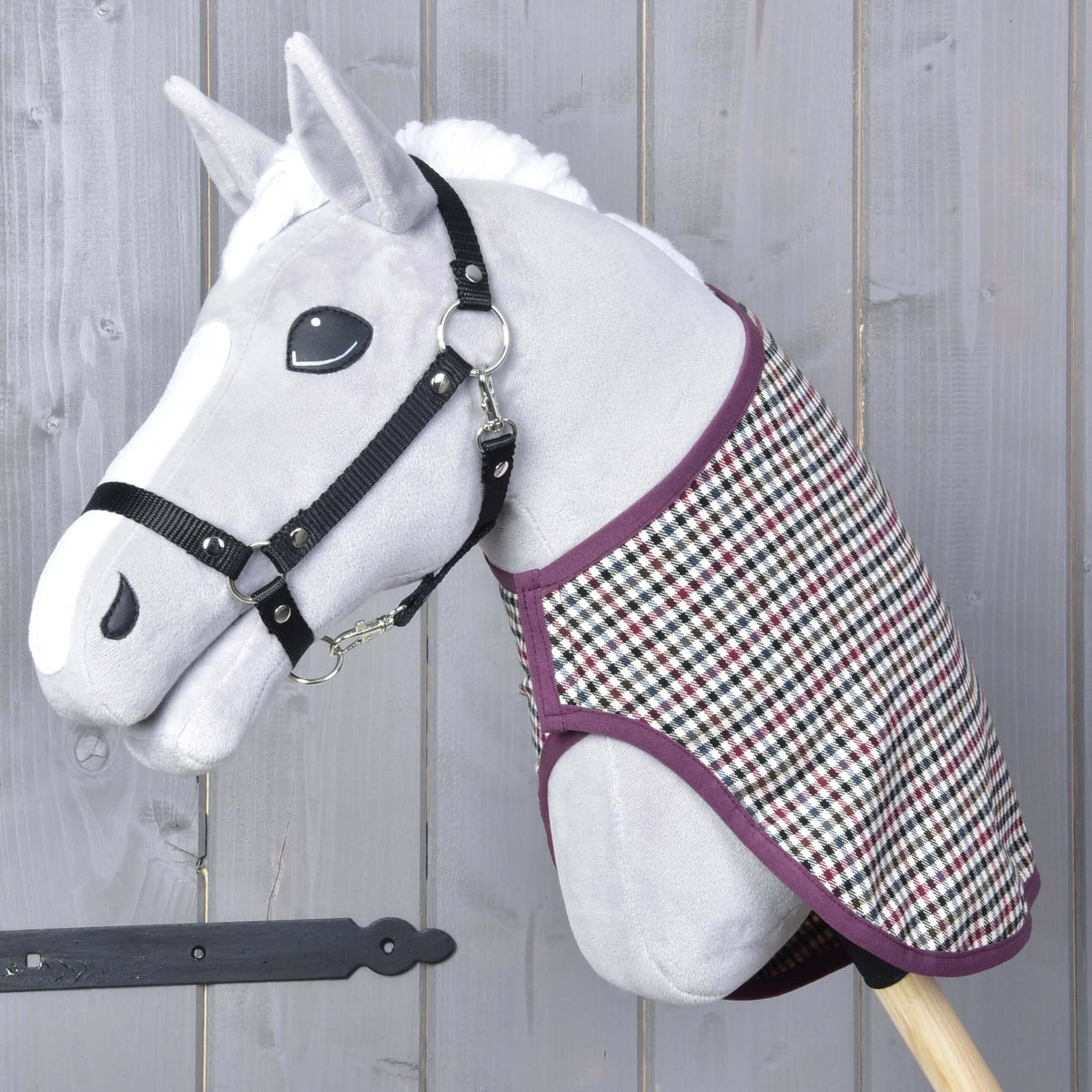 Sivá hračka Hobby Horse od Hobby Horse LarDen s čiernou ohlávkou a dekou western Colorado, nasadená na drevenej tyči a umiestnená pred sivou drevenou stenou.