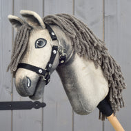 Hobby Horse Dusty s čiernou ohlávkou vo veľkosti XS od Hobby Horse LarDen s plyšovým hannoverským prevedením a sivou priadzovou hrivou je zobrazený na pozadí sivého dreva.