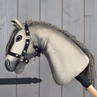 Hobby Horse Dusty s čiernou ohlávkou vo veľkosti XS od Hobby Horse LarDen má plyšovú hlavu hannoverského koňa s gombíkovými očami a čiernou ohlávkou, je nasadený na drevenej tyči a zobrazený na pozadí svetlého dreveného panelu.