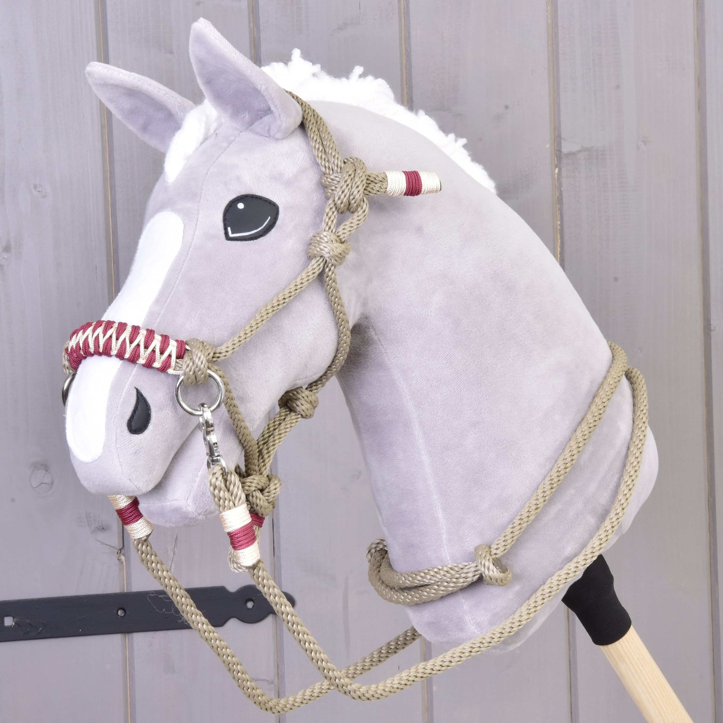 Sivý plyšový Hobby Horse s bielou hrivou a lysinou, ktorý má na sebe povrazový set Eleganza od Hobby Horse LarDen, stojí pred svetlou drevenou stenou.