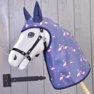 Pláštenka Flamingo od Hobby Horse LarDen, sivý Hobby Horse v tmavomodrej pláštenkovej kapucni s ružovými plameniakmi, je umiestnený pred drevenou stenou s čiernym kovovým pántom.