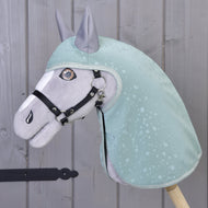 Hobby Horse LarDen „Pláštenka Greeny“ na plyšovom koni oblečenom v zelenej pláštenke so vzorom kvapiek vody a s čiernou uzdečkou, stojacom pri sivej drevenej stene. Vyšívané detaily a vztýčené uši ponúkajú zábavnú hru za každého počasia.
