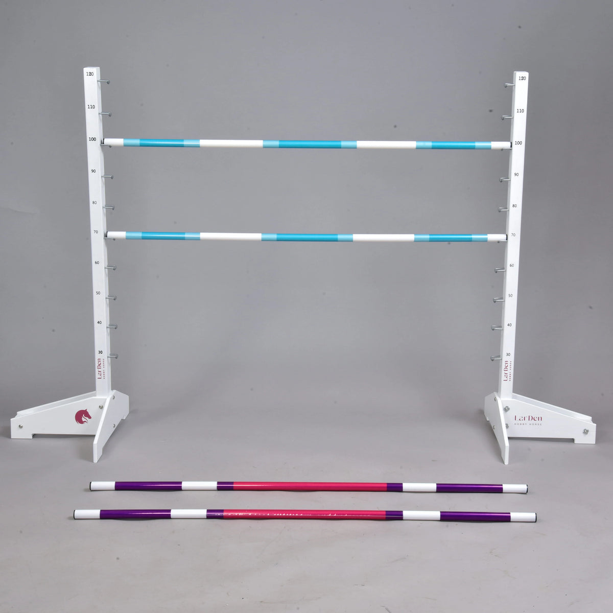 Set prekážky kolmák 120 cm + 2 ks bariérky od Hobby Horse LarDen s bielym nastaviteľným stojanom nesúcim dve modrobiele pruhované tyče a červené a fialové bariérky na sivej podlahe. Ideálny pre Hobby Horsing, s jednoliatym sivým pozadím.