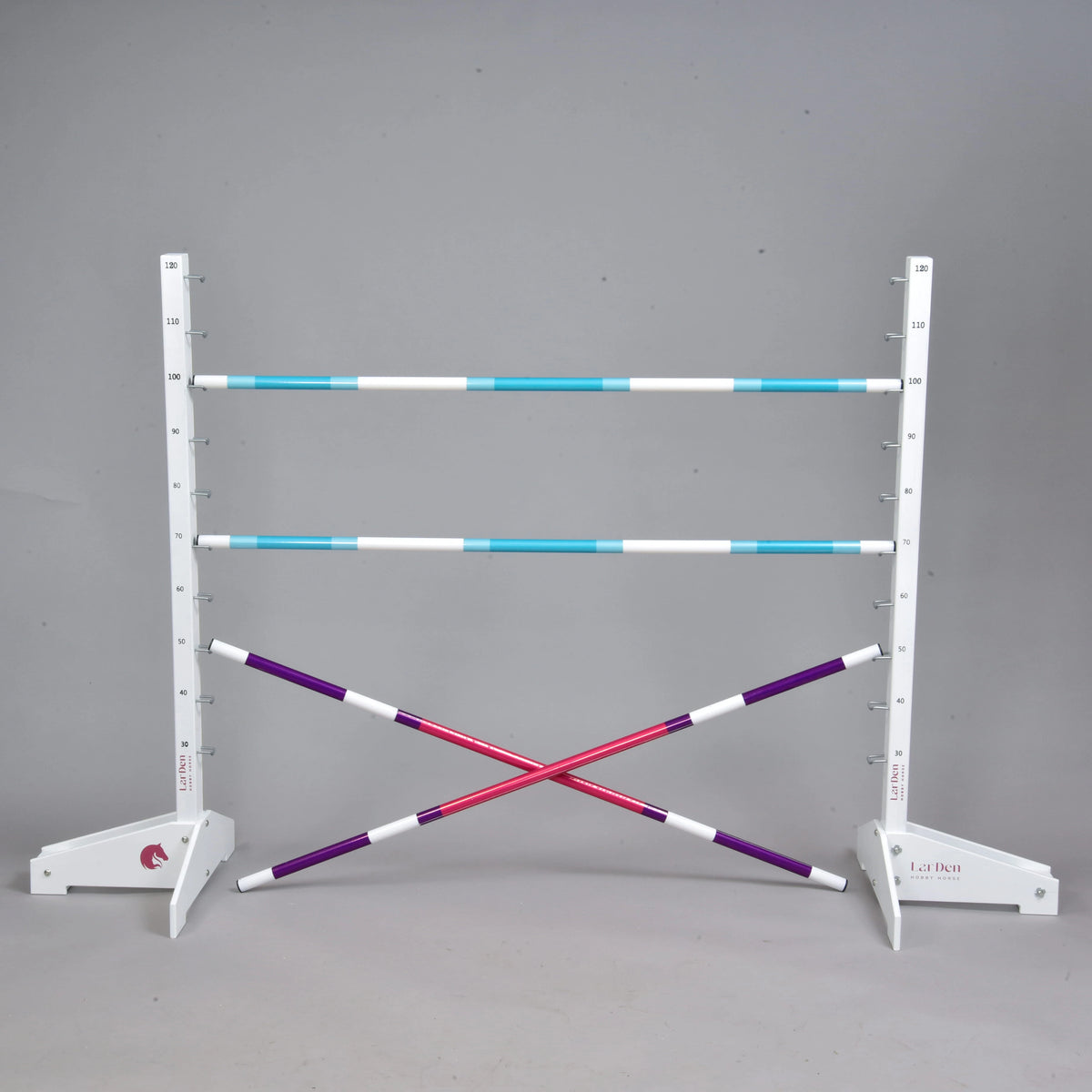 Set prekážky kolmák 120 cm + 2 ks bariérky od Hobby Horse LarDen obsahuje dva biele stojany, tri modrobiele nastaviteľné tyče, dve krížom položené fialovobiele tyče a je ideálny pre Hobby Horsing vnútri aj vonku. Zobrazené na jednoliatom sivom pozadí.