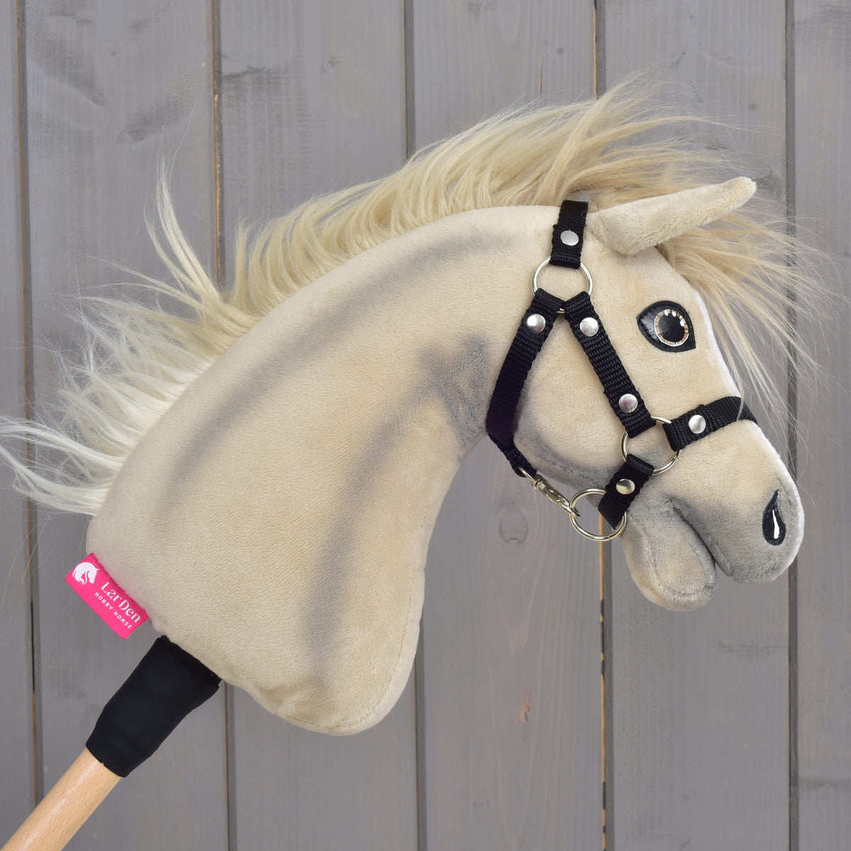 Detail Hobby Horse Ivory Dream s čiernou ohlávkou – veľkosť XS od Hobby Horse LarDen s béžovým plyšovým prevedením, čiernou ohlávkou a visačkou na krku na pozadí drevených dosiek.