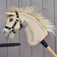 Hobby Horse Ivory Dream s čiernou ohlávkou – veľkosť XS od Hobby Horse LarDen s jemnou krémovou srsťou a drevenou tyčou, opretý o sivú drevenú stenu.