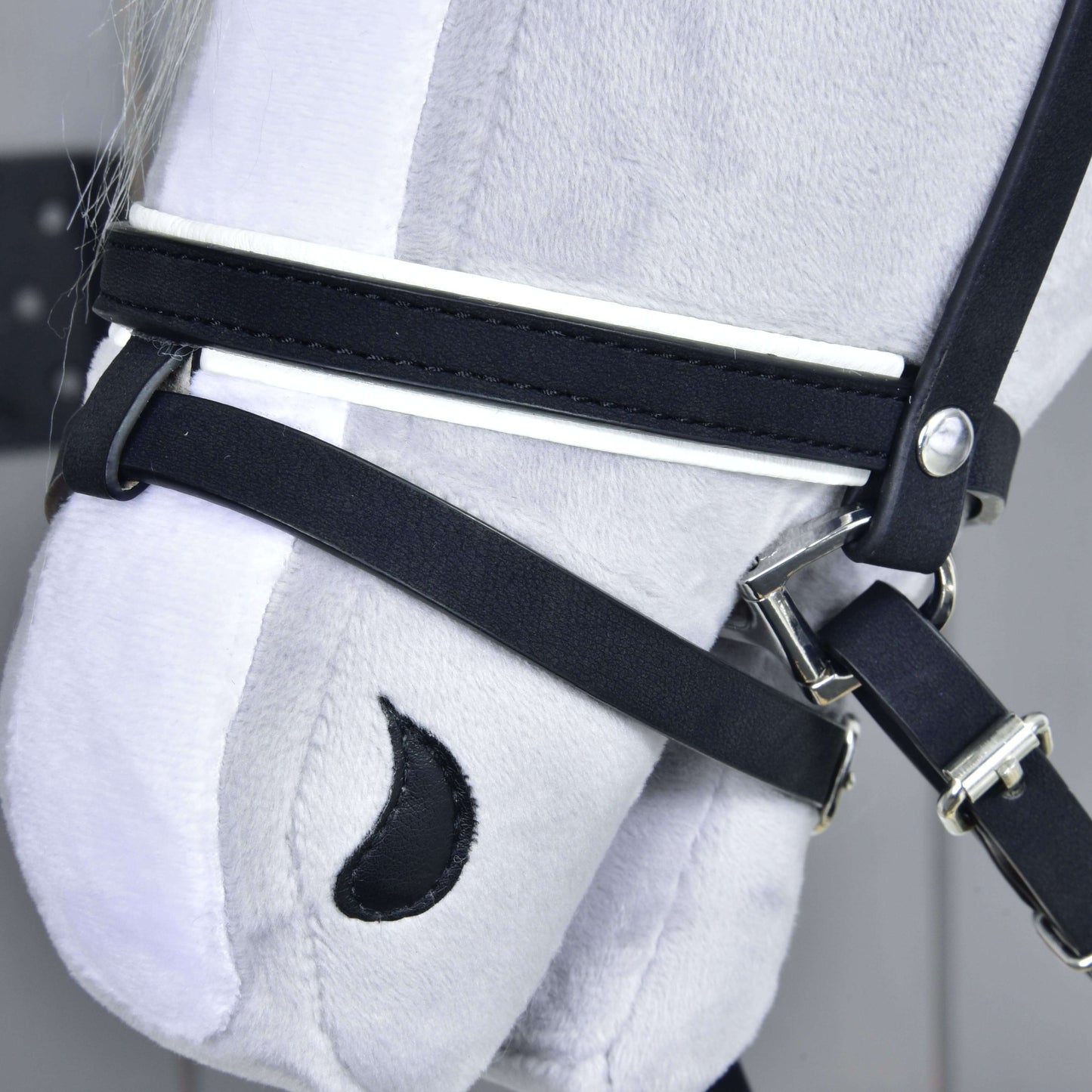 Detail hlavy sivého plyšového koňa od Hobby Horse LarDen s kompletnou uzdečkou De Luxe s 2 čelenkami. Vyšívané detaily, ako čierna nozdra v tvare polmesiaca, vynikajú na svetlom pozadí.