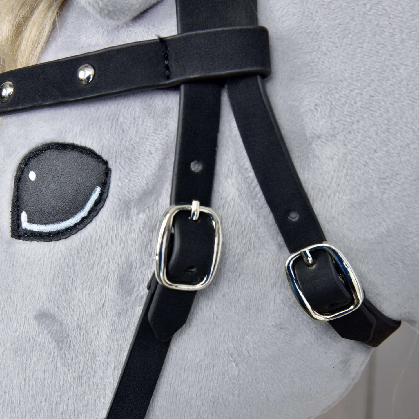 Detail Kompletnej uzdečky bezzubadlovej zdobenej od Hobby Horse LarDen – svetlá mäkká látka, vyšívané kreslené oko a čierne remienky z umelej kože s lesklými striebornými prackami a odnímateľnými opratami.