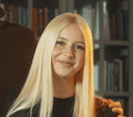 Mladá žena s dlhými rovnými blond vlasmi sa usmieva do kamery. Má na sebe čierny top a za ňou je rozmazaná knižnica. Ruka jej jemne spočíva na ramene, čo naznačuje vrelý okamih po zábavnom dni s Hobby Horsingom.