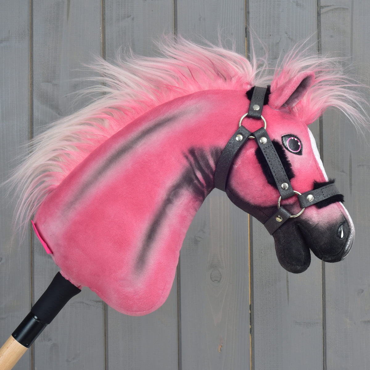 Limitovaná edícia Hobby Horse LarDen Pinkie s trblietavou ohlávkou a drevenou tyčou, umiestnená pred pozadím zo sivých drevených panelov.