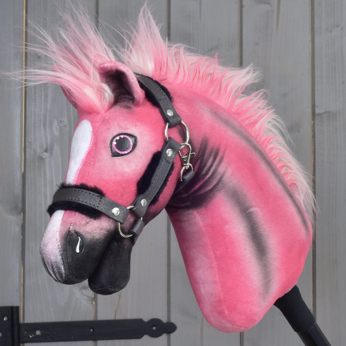 Limitovaná edícia Hobby Horse LarDen Pinkie s trblietavou ohlávkou, s huňatou hrivou a bielou škvrnou na tvári, umiestnená pred sivými drevenými panelmi.
