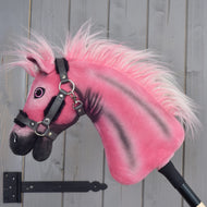Limitovaná edícia Hobby Horse LarDen Pinkie s trblietavou ohlávkou od Hobby Horse LarDen, nasadená na tyči a umiestnená pred sivou drevenou stenou.