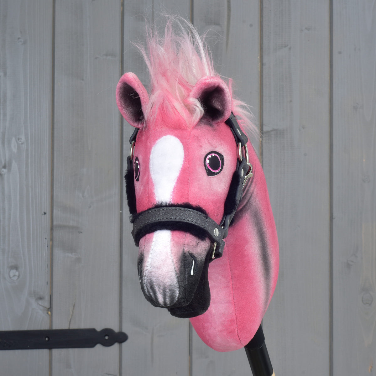 Limitovaná edícia Hobby Horse LarDen Pinkie s trblietavou ohlávkou, s ružovobielym plyšom a huňatou ružovou hrivou, umiestnená pred sivým dreveným pozadím.