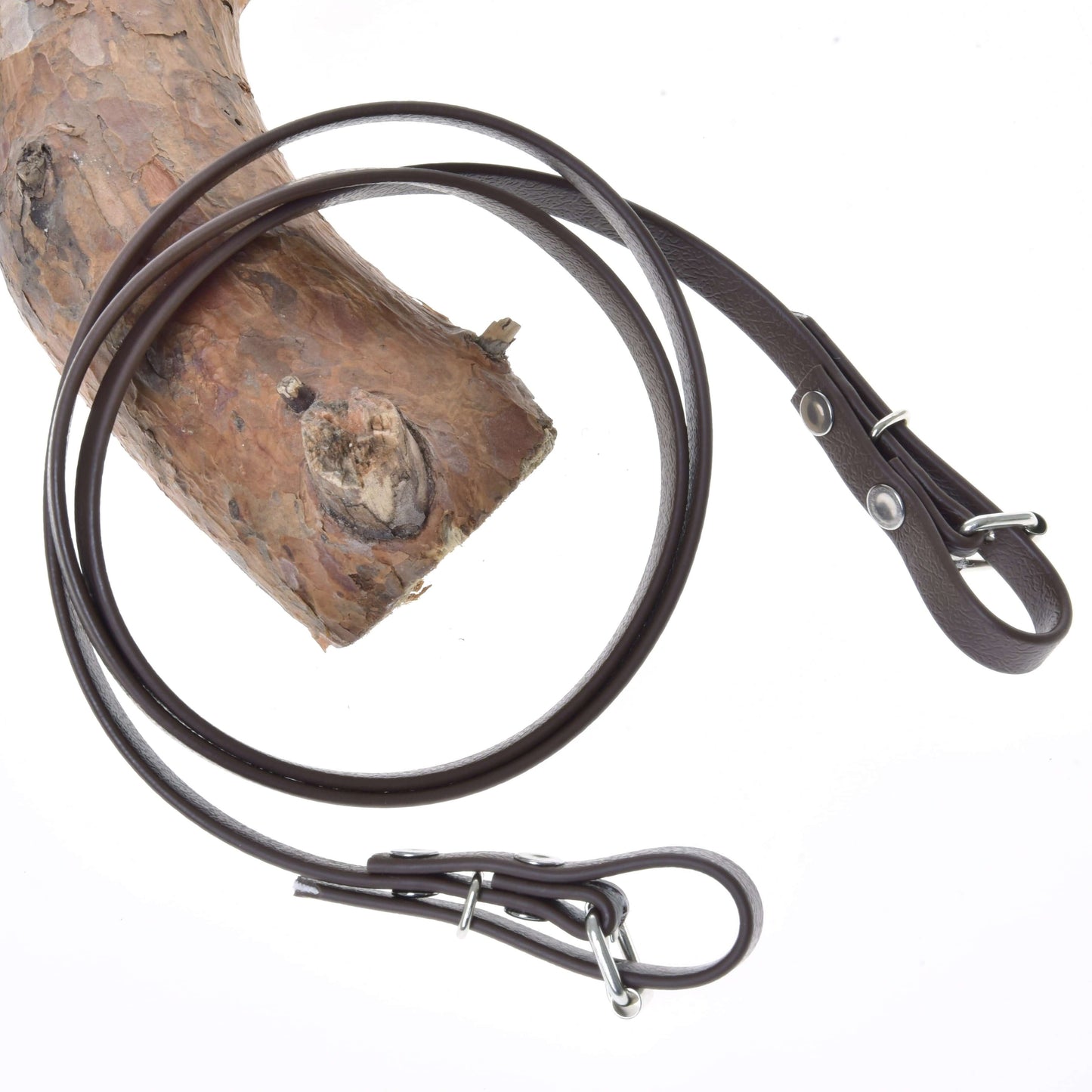 Opraty Light brown od Hobby Horse LarDen sú prehodené cez textúrovanú vetvu stromu na bielom pozadí a zvýrazňujú svoj štýlový kožený vzhľad a kovové kovanie pripomínajúce opraty k bezzubadlovej uzdečke.