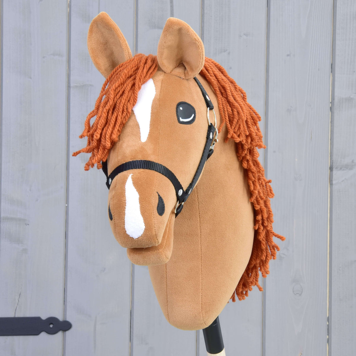 Hobby Horse Little Angel s čiernou ohlávkou od Hobby Horse LarDen má vzhľad ryšiaka českého teplokrvníka, bielu lysinu a biele znaky na nose, oranžovú hrivu z priadze a je zobrazený na svetlosivom drevenom pozadí.