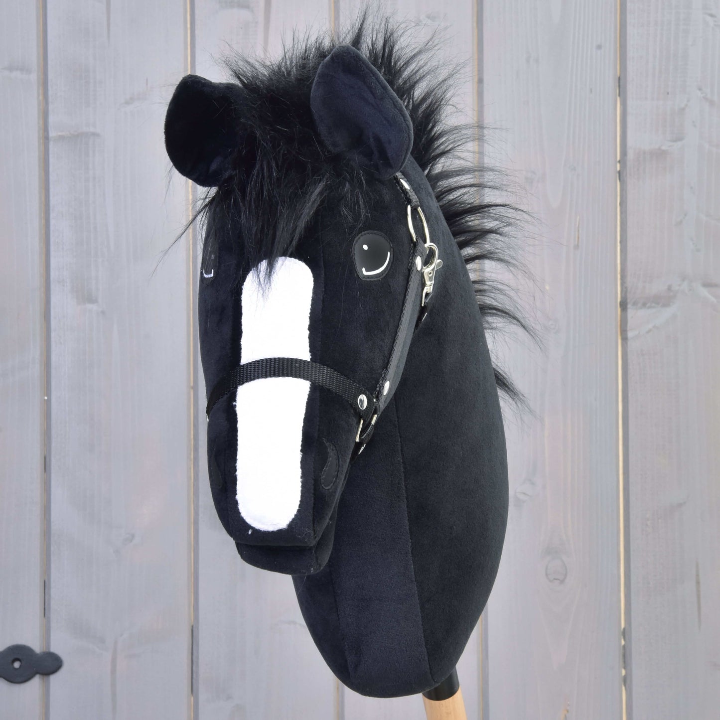 Hobby Horse Loki s čiernou ohlávkou od Hobby Horse LarDen má čierne plyšové prevedenie v štýle Welsh Coba, biely ňufák, huňatú hrivu a drevenú tyč – ideálny pre drezúrnu hru pred svetlosivým plotom.