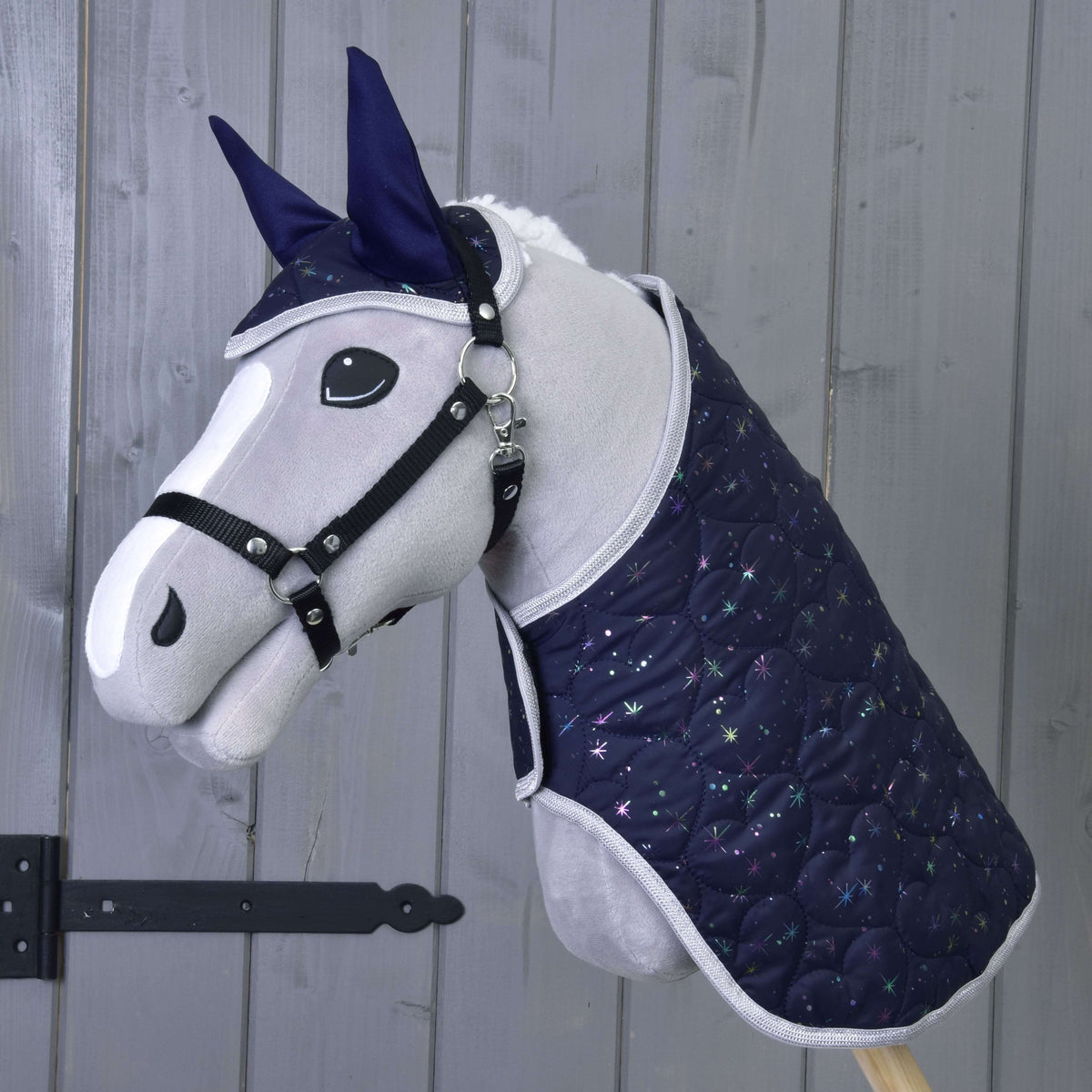 Hobby Horse LarDen Set Magic obsahuje plyšového Hobby Horse s tmavomodrou prešívanou dekou a náušníkom so vzorom hviezd, poskytujúci ochranu proti hmyzu, zobrazeného pred drevenou stenou.