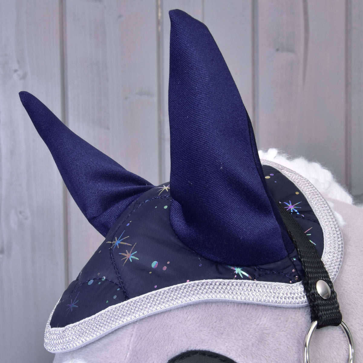 Detail Hobby Horse LarDen Set Magic: plyšová konská hlava s modrým náušníkom s trblietavým hviezdnym vzorom a bielym lemovaním pre ochranu proti hmyzu na svetlom drevenom pozadí.