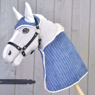 Set Manchester Plum od Hobby Horse LarDen obsahuje plyšového Hobby Horse s bielou tvárou, čiernou uzdečkou a modrým prešívaným prehozom plus ladiacu čabraku, naaranžované pred svetlou drevenou stenou.