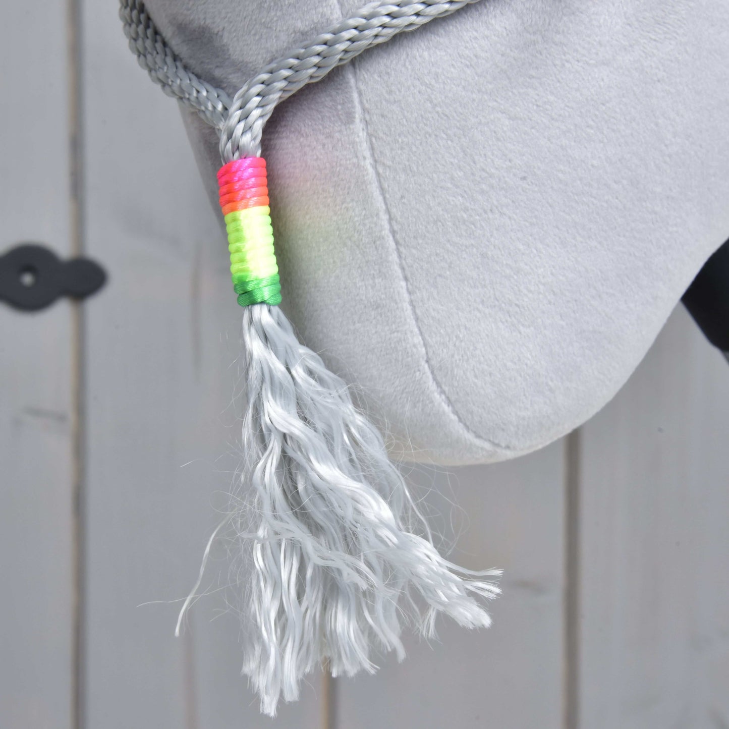 Detail sivej plyšovej hrivy Hobby Horse LarDen z Povrazového setu Manhattan s pletenou časťou omotanou jasnou viacfarebnou niťou, visiacej na svetlom drevenom pozadí.
