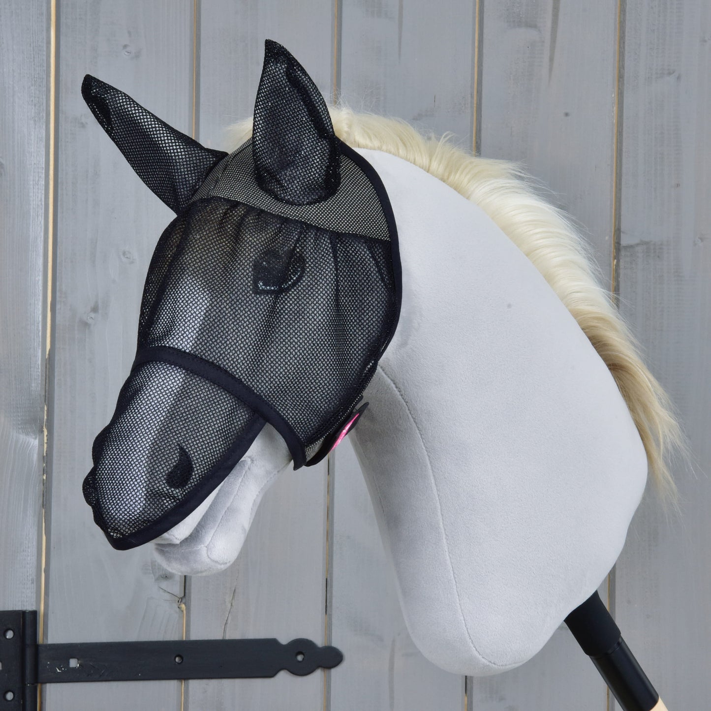 Maska proti hmyzu de Luxe Full od Hobby Horse LarDen na bielom Hobby Horse so svetlou hrivou, ktorého tvár chráni čierna sieťovina, na drevenom pozadí.