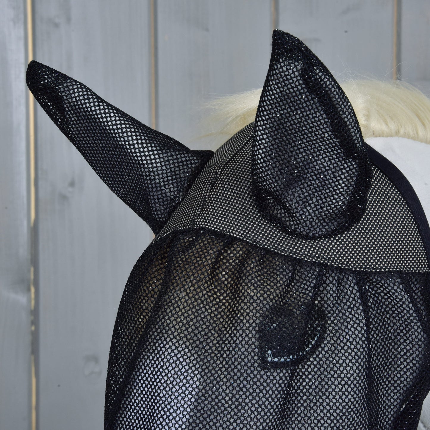 Detail koňa s maskou proti hmyzu de Luxe Full od Hobby Horse LarDen s krytmi uší, pred sivým dreveným pozadím.