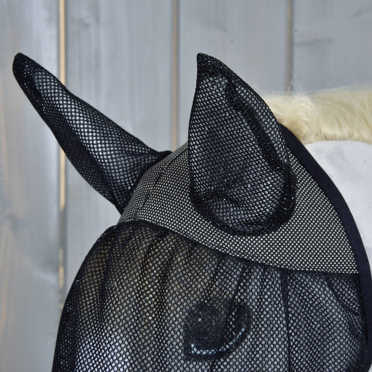 Detail konskej hlavy s maskou proti hmyzu de Luxe Full od Hobby Horse LarDen pre ochranu, s drevenou stenou v pozadí.