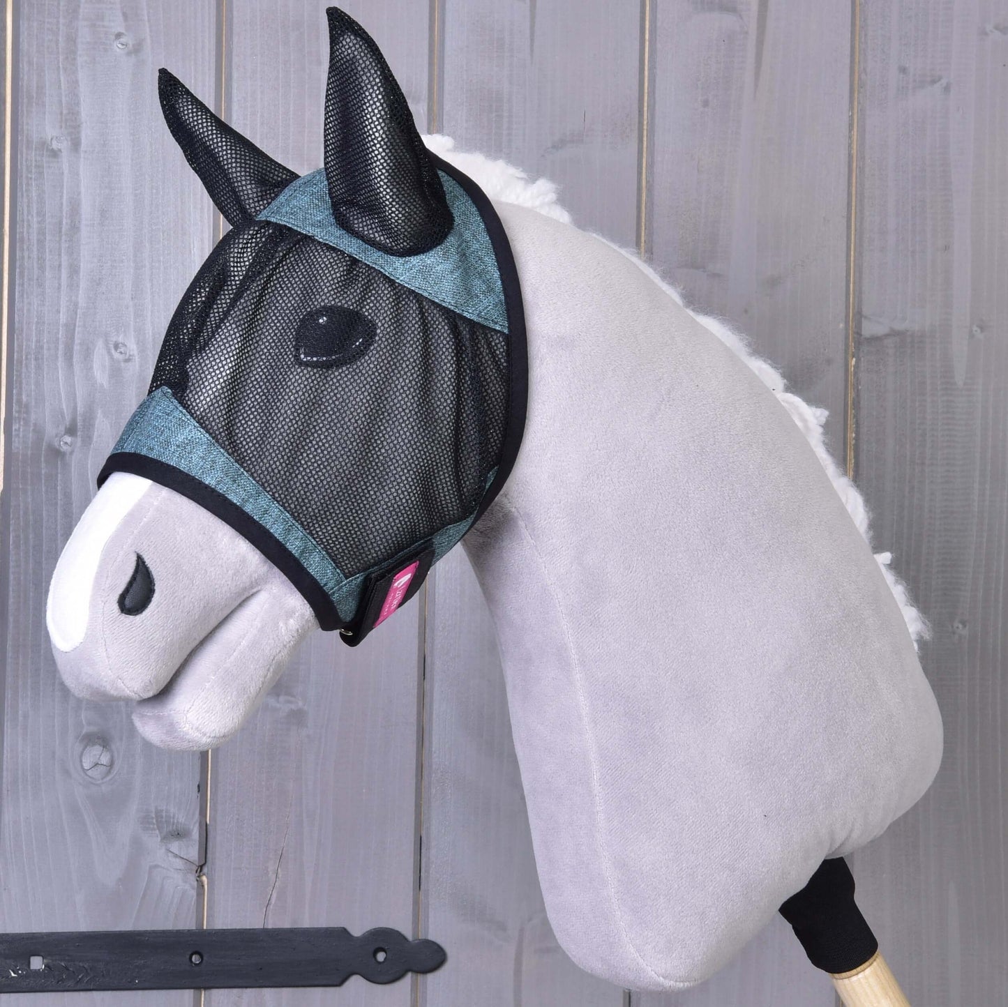 Maska proti hmyzu de Luxe Turquoise od Hobby Horse LarDen je nasadená na sivom plyšovom Hobby Horse s bielym ňufákom, pózujúcom pred drevenými doskami. Umývateľná maska poskytuje štýlovú ochranu pre tvoj Hobby Horse.
