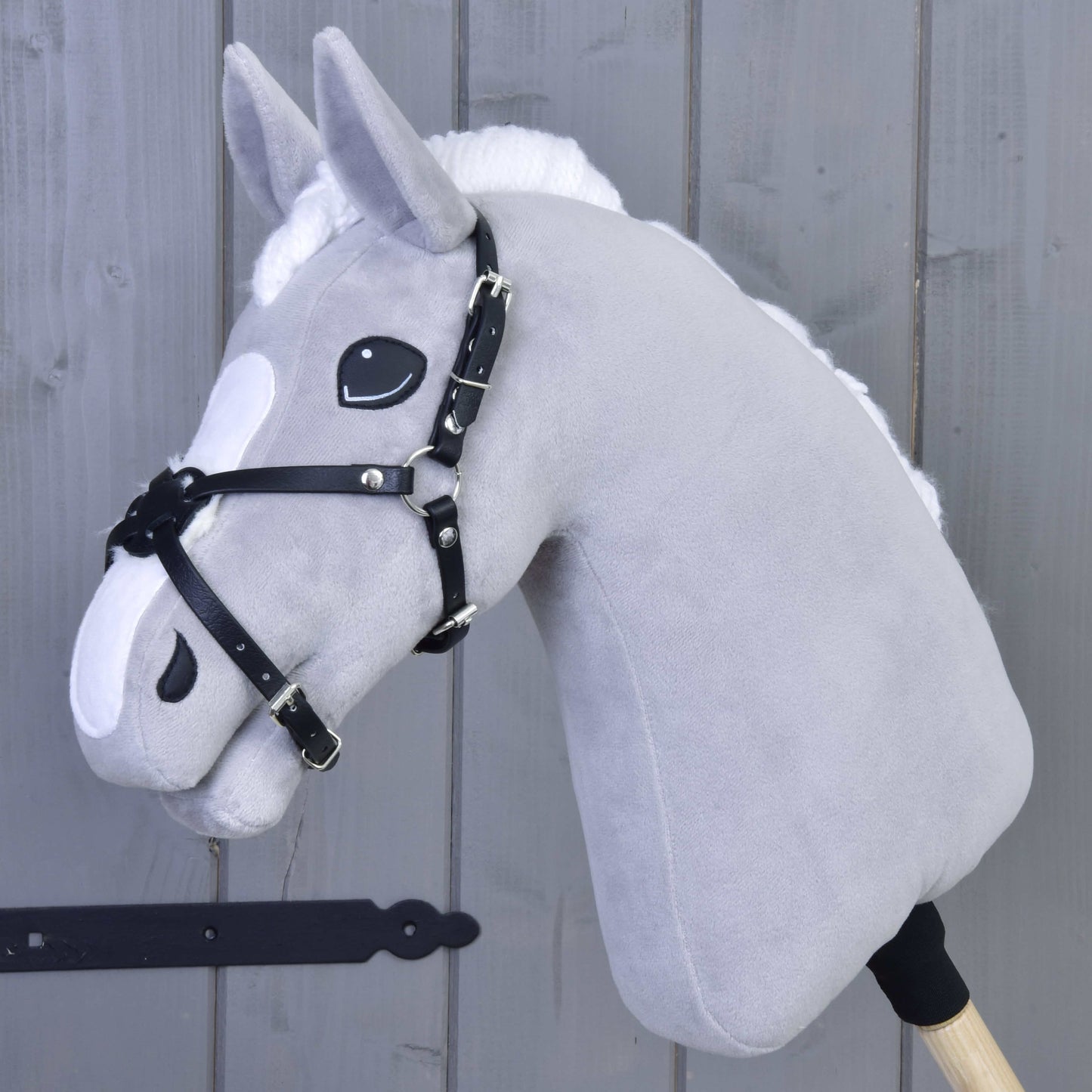Mexický nánosník čierny podšitý od Hobby Horse LarDen na sivom plyšovom Hobby Horse s bielou hrivou, čiernou uzdečkou a nánosníkom z koženky, na drevenej tyči pred sivým dreveným obloženým pozadím.