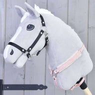Poprsník s barančekom Mullbery od Hobby Horse LarDen na sivom plyšovom Hobby Horse s bielou hrivou, čiernou uzdečkou, ružovou ohlávkou a mäkkým poprsníkom s kožušinovou podšívkou na drevenej tyči, na svetlosivom drevenom pozadí.