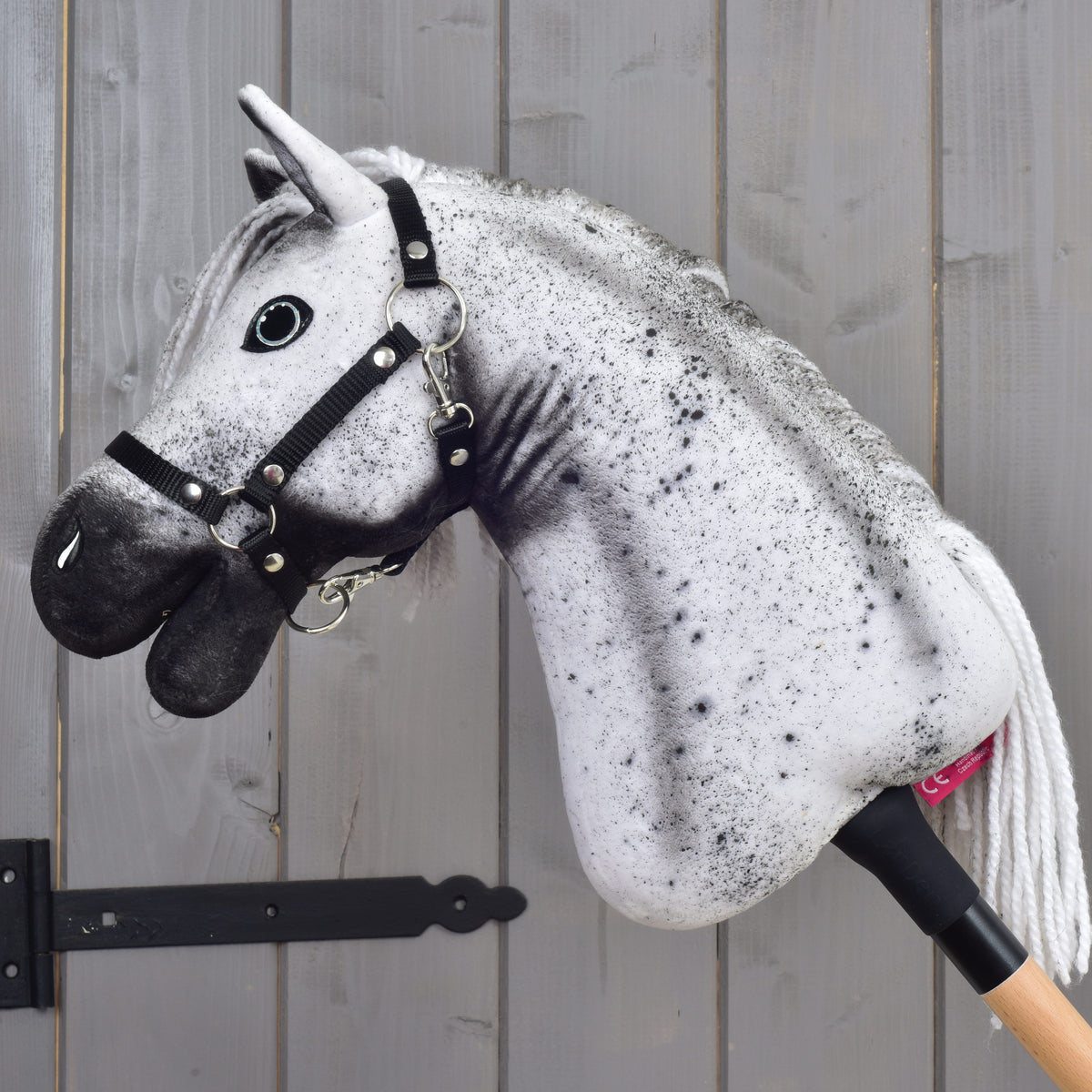 Hobby Horse Naivy s čiernou ohlávkou - veľkosť S od Hobby Horse LarDen, s realistickou sivo-čiernou hlavou žrebca a čiernou ohlávkou, vystavený pred sivou drevenou stenou.