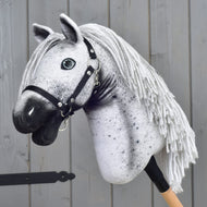 Hobby Horse LarDen "Hobby Horse Naivy with Black Halter" (velikost S), se šedo-bílým appaloosa vzhledem, černou ohlávkou a přízovou hřívou, nasazený na dřevěné tyči a umístěný před šedou dřevěnou stěnou.